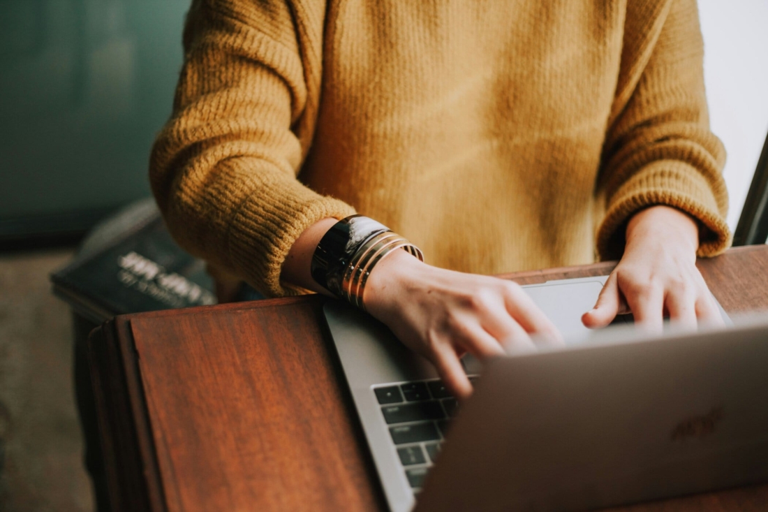 Persoon werkt aan laptop met notitieboekje op tafel.